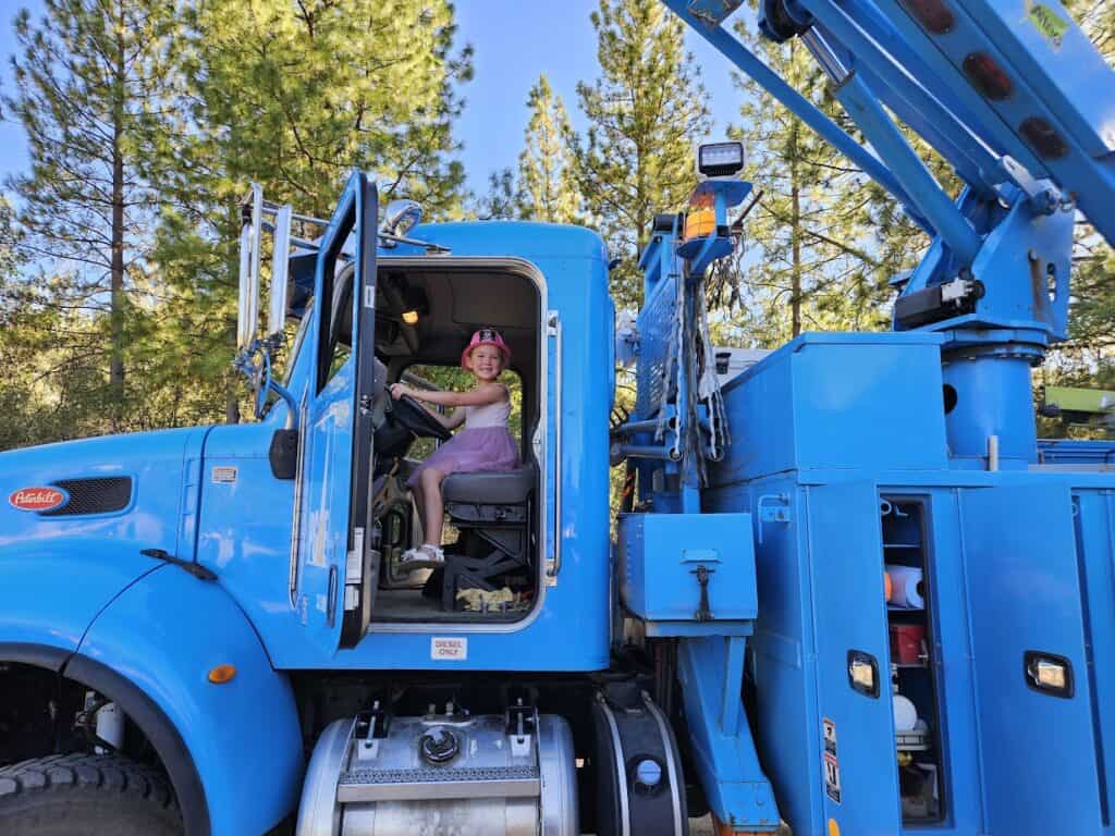 Juvenile girl sitting in blue utility truck seat at El Dorado Adventist School, outdoors.