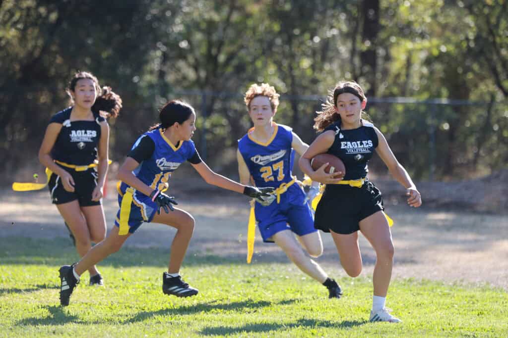 Young girls playing flag football at El Dorado Adventist School during a sports event.