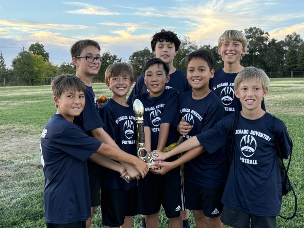 Children holding a football trophy, celebrating football victory at El Dorado Adventist School sports event.