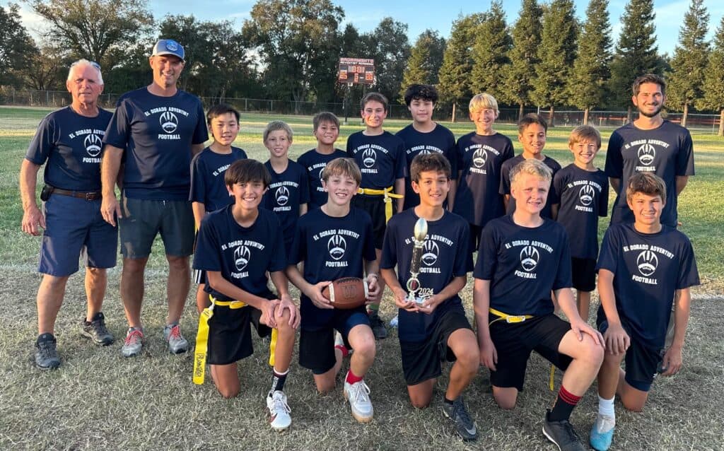El Dorado Adventist School football team with coach celebrating victory outdoors.