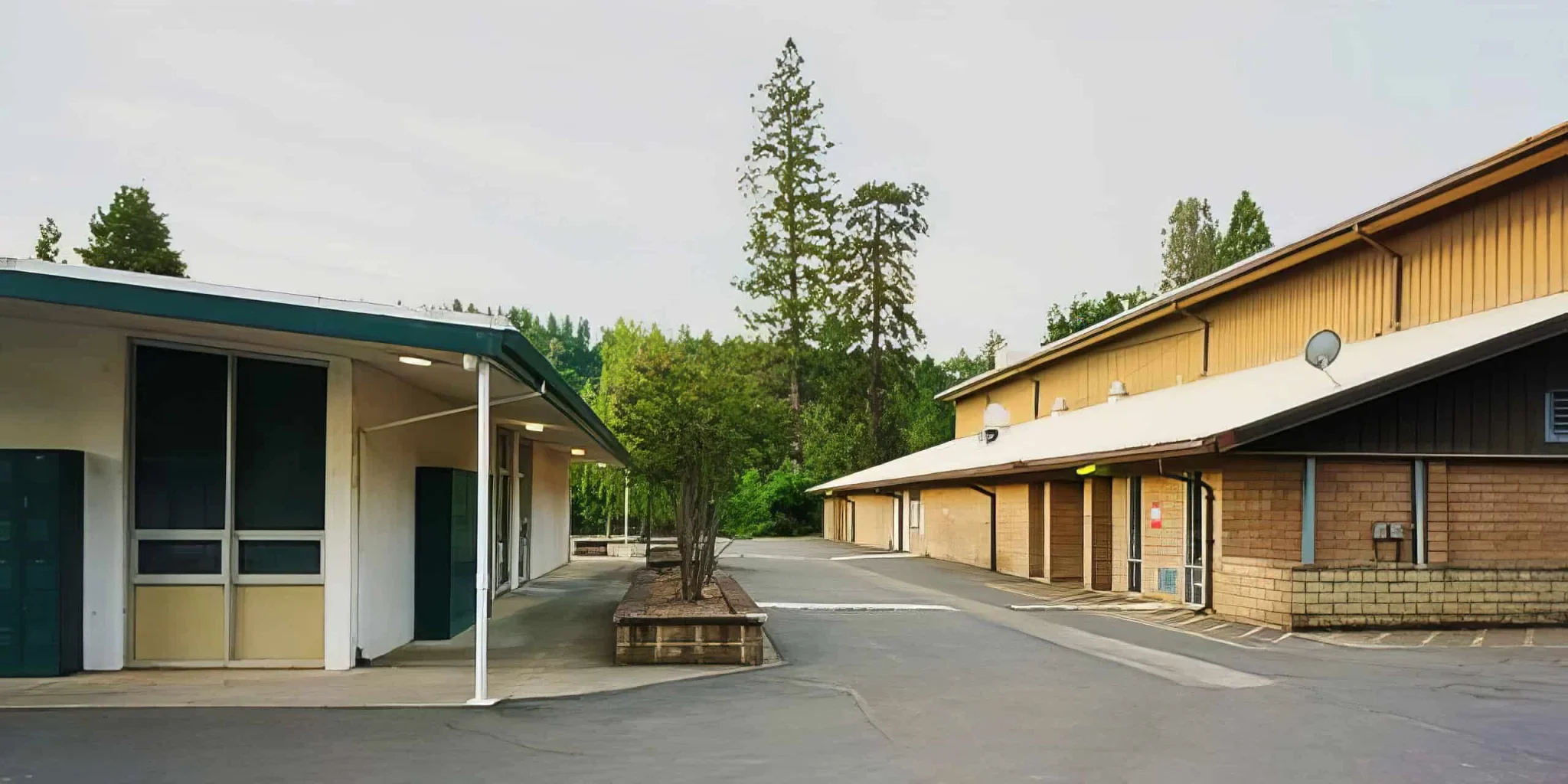Stone buildings of El Dorado Adventist School with surrounding trees and parking lot in sunny weather.