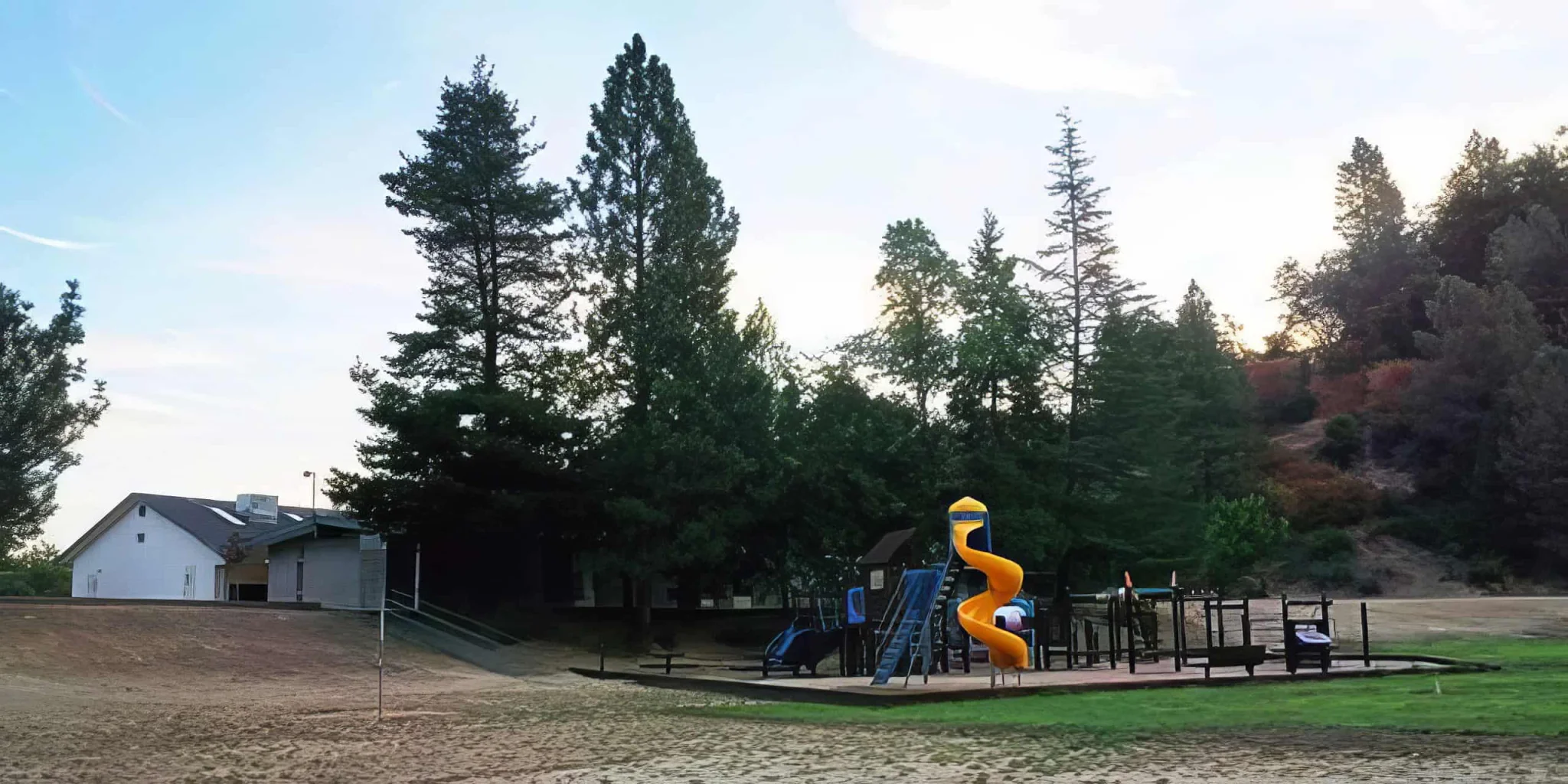 Playground with slides and benches at El Dorado Adventist School amidst tall trees and natural scenery.