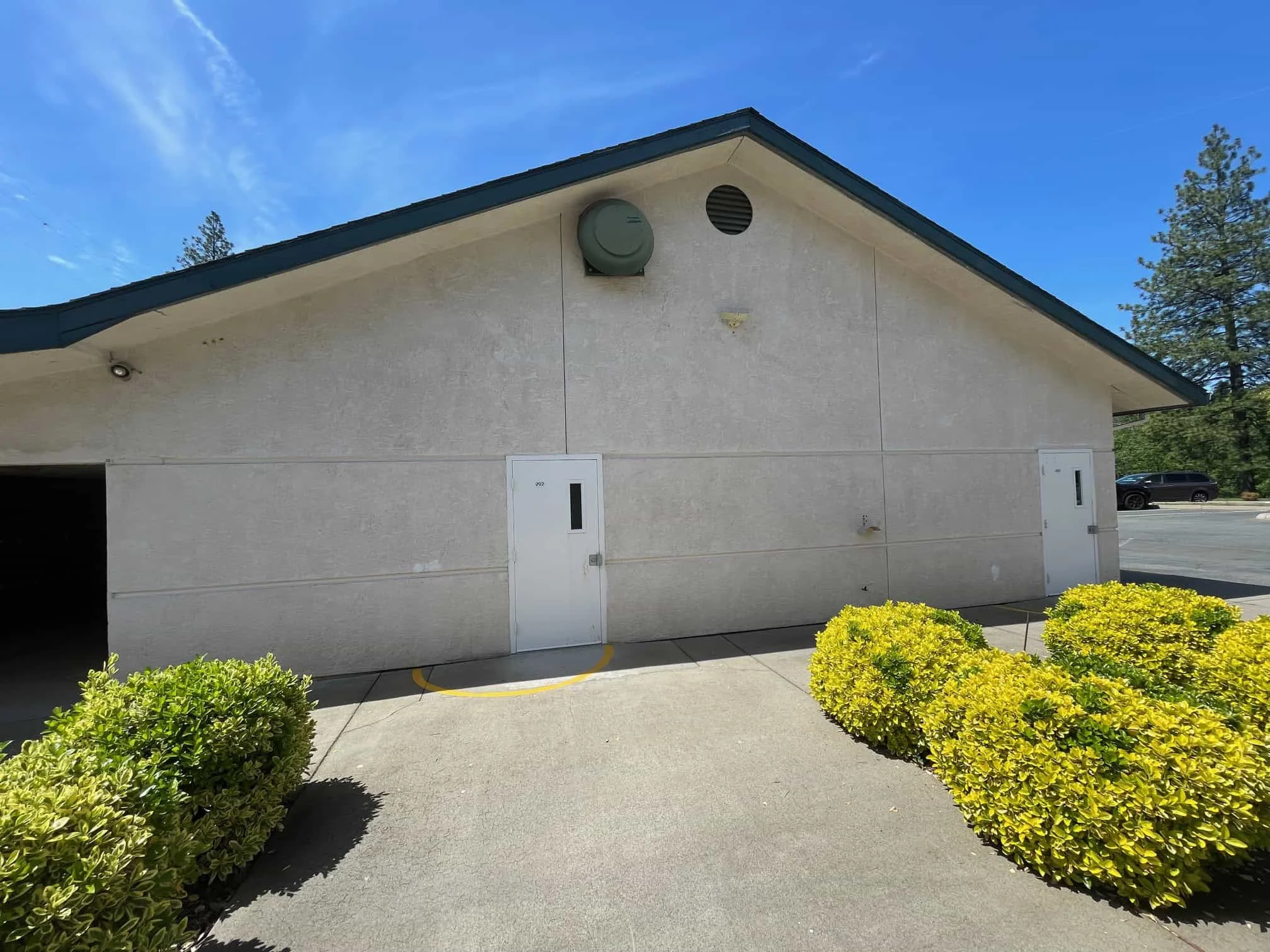 Modern school building exterior at El Dorado Adventist School with landscaped bushes and bright blue sky.